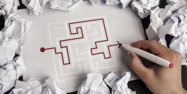 A hand holds a red marker and traces the path of how to escape from a maze.